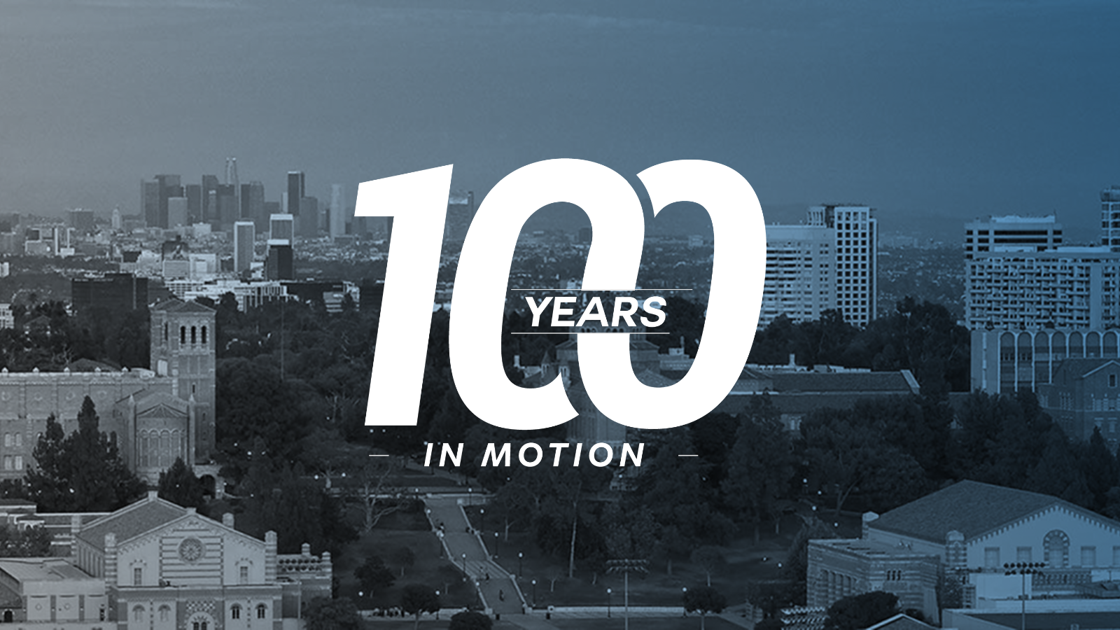 An aerial image of UCLA campus facing eastward. The Los Angeles downtown skyline visible in the background. Over a blue-to-grey gradient sits a large logo for "100 Years in Motion"